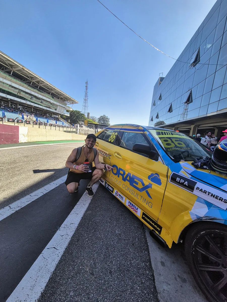 Danilo agachado ao lado de um carro de corrida amarelo em Interlagos
